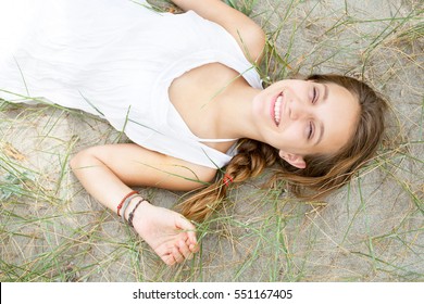 Portrait Of Beautiful Teenager Girl Laying Down On Sand Dunes On Beach, Relaxing Looking At Camera, Smiling Outdoors. Healthy Young Woman On Summer Holiday, Recreational Lifestyle, Nature Exterior.