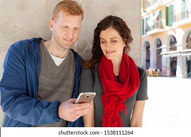 Portrait Of Beautiful Tourist Couple On Sunny Winter City Break Holiday Sightseeing Together, Using Technology Smartphone Smiling Outdoors. Fun Travel Vacation, People Leisure Recreation Lifestyle.