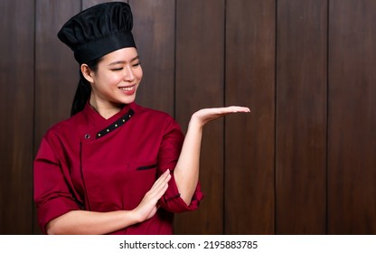 Portrait Beautiful Traditional Professional Chinese Chef Wearing Red Uniform, Hat, Happily Smiling, Raising Hand Showing, Presenting Blank Copy Space For Advertisement. Restaurant, Food Concept