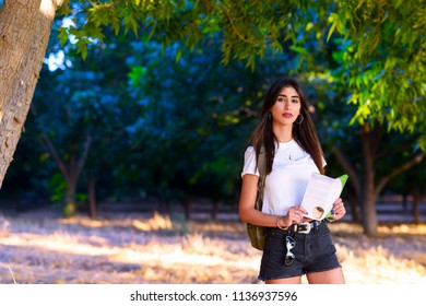 Portrait Of Beautiful Traveler Girl Hiker Tourist Holding Travel Guide Book, Standing In The Magic Sunny Forest, Concept Of Journey Travel, Vacation, Healthy, Personal Development,  Loving Yourself. 