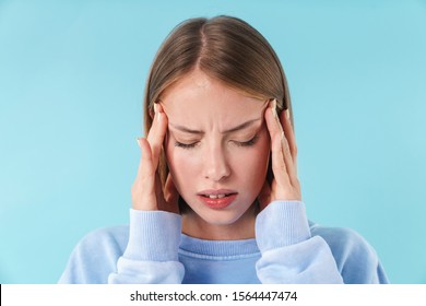 Portrait of a beautiful upset young blonde short haired woman wearing sweatshirt standing isolated over blue background, suffering from a headache