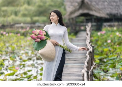 Portrait of beautiful vietnamese woman with traditional vietnam hat holding the pink lotus walking on the wooden bridge in big lotus lake, vietnam, aisan or southeast asia travel concept