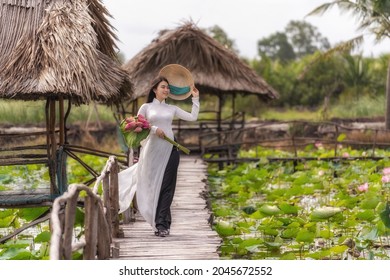 Portrait of beautiful vietnamese woman with traditional vietnam hat holding the pink lotus walking on the wooden bridge in big lotus lake, vietnam, aisan or southeast asia travel concept