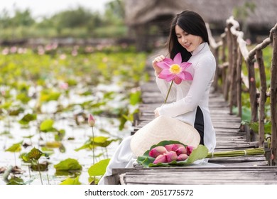 Portrait of beautiful vietnamese woman with traditional vietnam hat holding the pink lotus sitting on the wooden bridge in big lotus lake, vietnam, aisan or southeast asia travel concept