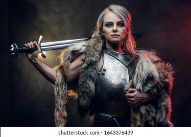 Portrait of a beautiful warrior woman holding a sword wearing steel cuirass and fur. Fantasy fashion. Studio photography on a dark background. Cosplayer as Ciri from The Witcher.