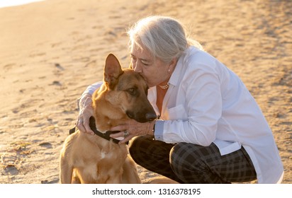 Portrait Of Beautiful Widow Older Woman And German Shepard Dog Enjoying Its Companion And Love On Beach In Benefits Of Animals Active Retirement Lifestyle And Dog Friendly Tourism In Afternoon Light.