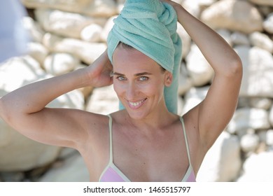 Portrait of beautiful woman after bathing. Attractive female person in turban from towel posing against masonry. She corrects turban and looks at camera smiling - Powered by Shutterstock