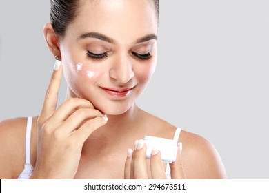 portrait of beautiful woman applying some cream to her face for skin care