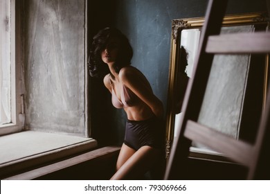 Portrait Of Beautiful Woman In Black Shorts And A White Shirt, With Curly Black Hair Posing In An Old Interior. Beautiful Woman In Erotic Lingerie. Vintage Photo Procession