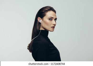 Portrait Of Beautiful Woman In Black Top Wearing Earphones Staring At Camera. Studio Shot Of Young Beautiful Woman As Secret Agent Against Grey Background.