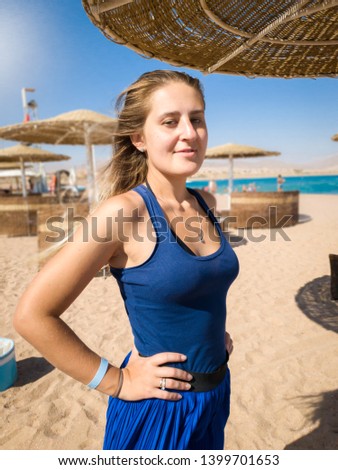 Portrait of beautiful woman in blue shirt and short skirt standing on the sea beach at sunny windy day