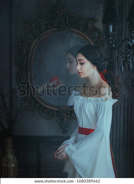 Portrait beautiful woman concept sleeping beauty\
fairytale Snow White. medieval clothes dress. Gothic princess\
makeup red lips. Ghost female hand with poison apple is reflected\
vintage antique mirror