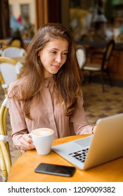 Portrait of a beautiful woman in a cozy cafe with cup of cappuccino and laptop.
