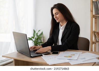 Portrait Of A Beautiful Woman Data Analyst Sitting At A Desk Working On A Laptop. Stylish Woman In An Office Setting. Searching For New Solution