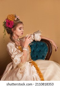 Portrait of beautiful woman dressed in period rococo fashion as Marie Antoinette holding a glass and sitting on her blue chair - Shutterstock ID 2110818353