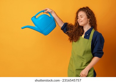 Portrait of a beautiful woman gardener with watering can against yellow background - Powered by Shutterstock