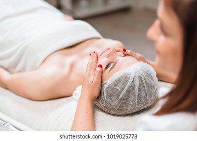 Portrait of a beautiful woman having a facial massage beauty treatment made by a professional doctor-cosmetologist in a beauty salon. - Shutterstock ID 1019025778
