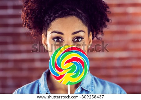 Portrait of a beautiful woman holding a giant lollipop against a brick background