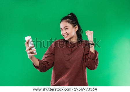 Portrait beautiful woman holding and look handphone with happiness expression while raising one hand and making a fist, isolated on green background