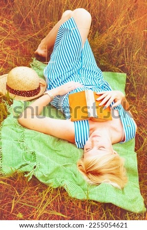 Portrait of beautiful woman lies in the wild flowers field and looking. She was reading a book and fell asleep. Summer holiday, rest and education concept.