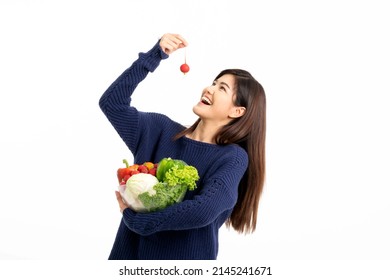 Portrait of a beautiful woman with long hair wearing a blue long-sleeve shirt trying to eat vegetables on a white background. Selective focus. - Shutterstock ID 2145241671