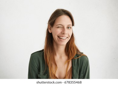 Portrait of beautiful woman with long hair winking while having good mood smiling showing her white perfect teeth. Brunette young female blinking her eye showing her sympathy or positiveness - Shutterstock ID 678355468