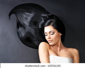 Portrait Of A Beautiful Woman With Long Straight Black Hair Lying On The Dark Background