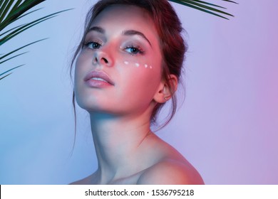 Portrait Of Beautiful Woman Looking At Camera With Calmness. Girl With Fresh And Clean Skin Applying Wrinkle Smoothing Cream For Skin Under Eye. Beauty And Cosmetics Concept. Blurred Background