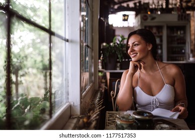 Portrait Of A Beautiful Woman Looking Through Window While Sitting In Conservatory Or Sunroom.