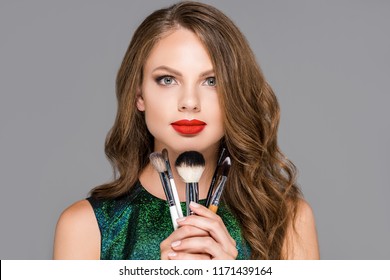 Portrait Of Beautiful Woman With Makeup Brushes Looking At Camera Isolated On Grey