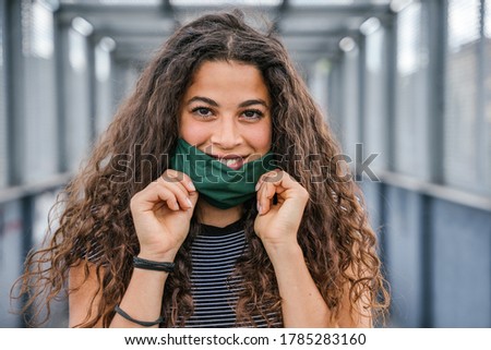 Portrait of beautiful woman on iron bridge in the summer in the city with face mask for protection from contagion by Coronavirus, Covid-19 - Millennial looking and smiling - Concept of naturalness