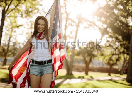 Portrait of a beautiful woman in the park with American flag. Smiling american girl holding national flag proudly and looking at camera.