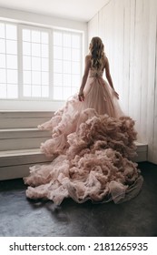 The Portrait Of Beautiful Woman In Pink Lush Long Dress In White Wooden Interior. Long Veil In Steps. Princess Style Girl. Birthday Party. Big Panoramic Windows.