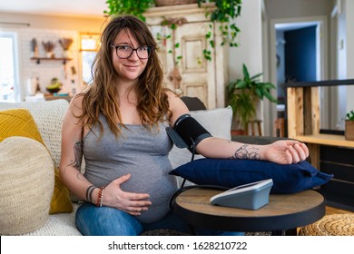 A Portrait Of A Beautiful Woman Preparing For Childbirth At Home, Heavily Pregnant With Swollen Tummy, Measuring Blood Pressure With A Cuff Monitor