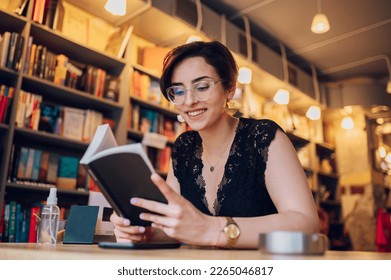 Portrait of beautiful woman reading a book while relaxing in the cafe. Young female customer reading a book in bookstore while buying some good literature. - Powered by Shutterstock