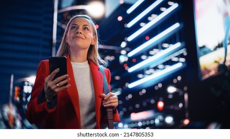 Portrait of a Beautiful Woman in Red Coat Walking in a Modern City Street with Neon Lights at Night. Attractive Female Using Smartphone and Looking Around the Urban Cinematic Environment. - Powered by Shutterstock