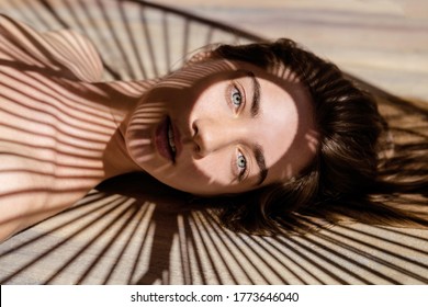 Portrait of beautiful woman with shadows of palm leaf on her face. Concept of sunbathing, vacation.