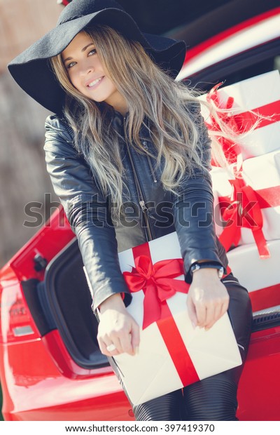portrait of beautiful woman sitting on car trunk\
full of gift boxes. presents for holidays. woman and luxury car.\
gifts. happiness.\
smile.