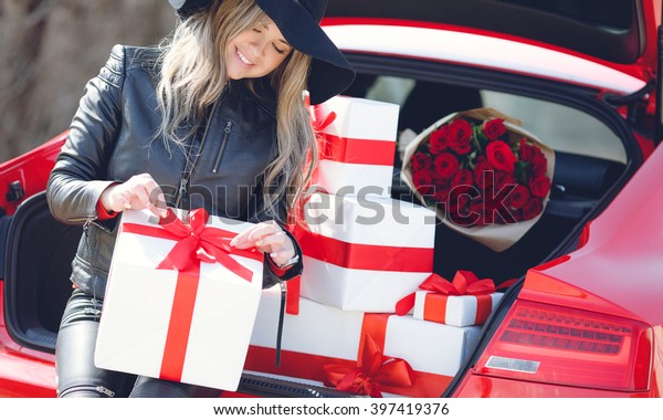 portrait of beautiful woman sitting on car trunk\
full of gift boxes. presents for holidays. woman and luxury car.\
gifts. happiness.\
smile.