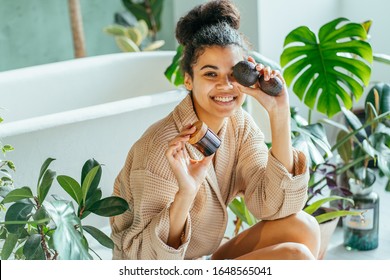 Portrait of beautiful woman smiling while taking some facial cream, holding jar with product and avocado. Beauty, cosmetics, skincare, zero waste, green, eco, natural conscious lifestyle concept.