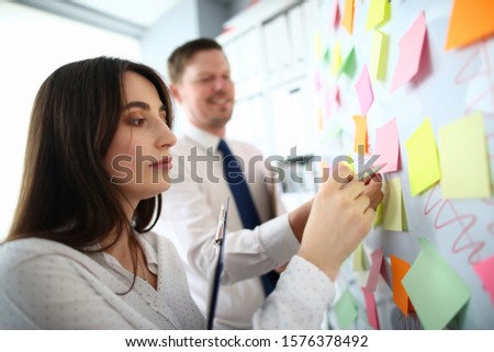 Portrait of beautiful woman sticking colourful notes on board at workplace. Co-workers making biz remarks. Business people preparing presentation. Business concept
