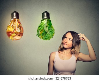 Portrait beautiful woman thinking looking up at junk food and green vegetables shaped as light bulb isolated on gray background. Diet choice right nutrition healthy lifestyle concept  
