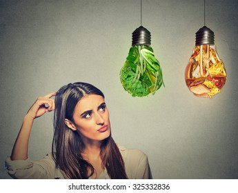 Portrait Beautiful Woman Thinking Looking Up At Junk Food And Green Vegetables Shaped As Light Bulb Isolated On Gray Background. Diet Choice Right Nutrition Healthy Lifestyle Concept  