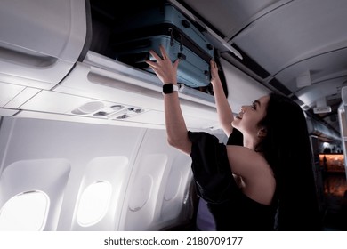 Portrait Beautiful Woman Tourist  Putting Her Hand Luggage Into Overhead Locker On Airplane ,when She Travel By Plane On Her Holidays.