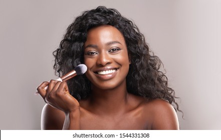 Portrait of beautiful woman using blush brush on face, applying makeup on gray studio background, panorama