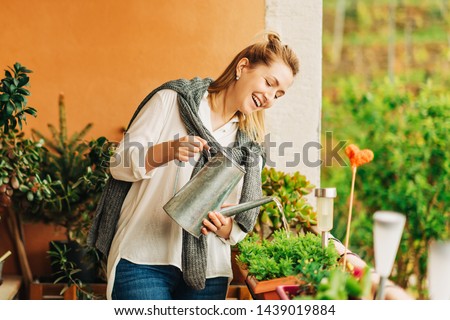 Portrait of beautiful woman watering green plants on the balcony, small cozy garden in apartment