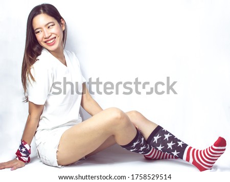 Portrait of beautiful woman wearing clothes decorated by american flag and sitting on white background for celebrating independence day on 4th of July. Symbol and Fashion concept.