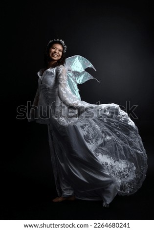 portrait of beautiful woman wearing  fantasy costume with white bridal gown  and translucent fairy wings.    Posing with gestural arms reaching out, isolated on black studio background.