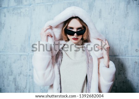 A portrait of a beautiful woman wearing a fur coat with hood and sunglasses. Beauty, winter fashion, style.