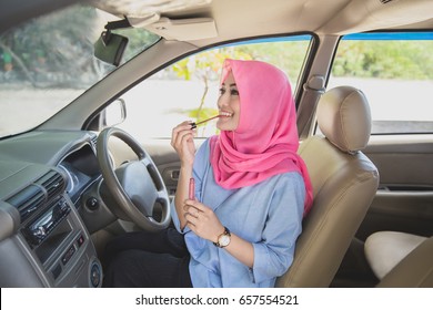 portrait of beautiful woman wearing hijab applying lipstick in the car